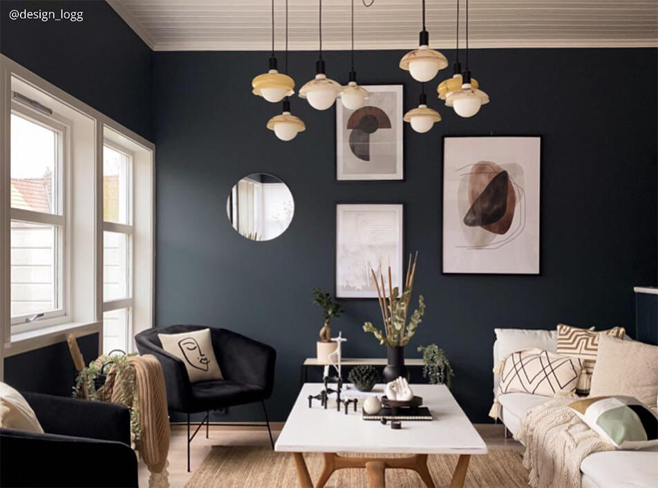 Salon z ciemnymi ścianami, czarne welurowe fotele, okrągłe lustro, graficzne plakaty